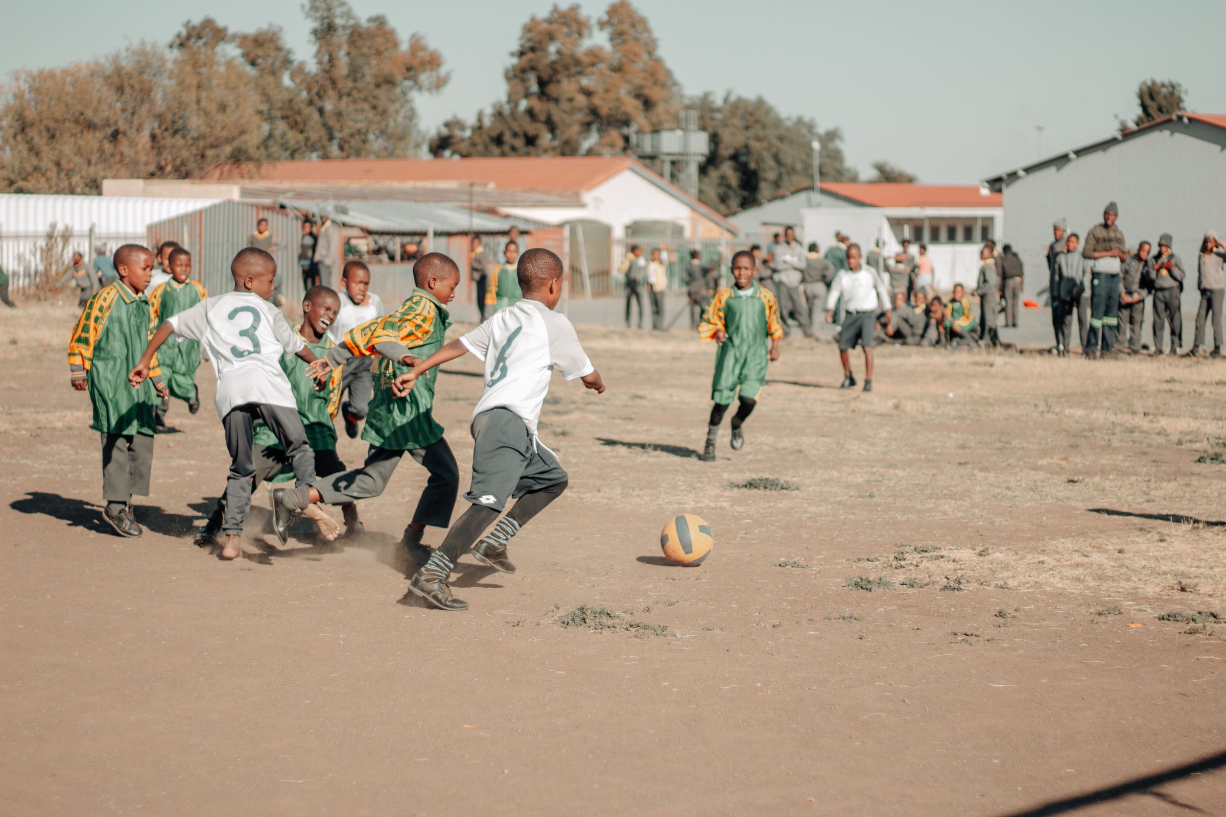 Children playing a football match on a dusty field in a South African township