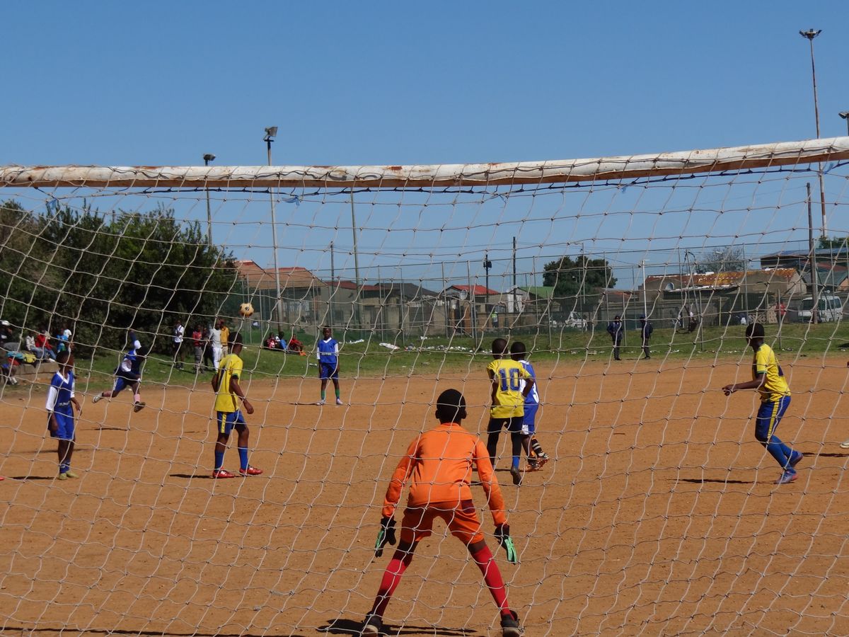 A youth match on a dusty pitch, the goalkeeper ready in goal